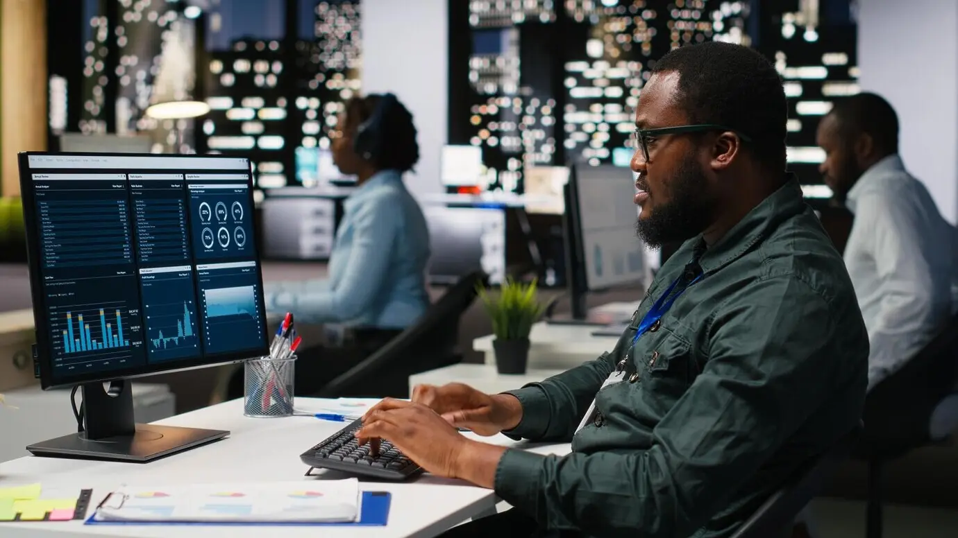 Büromitarbeiter überprüft KPI-Kennzahlen auf dem Monitor und Analysen auf dem Desktop, entwickelt eine Vision und